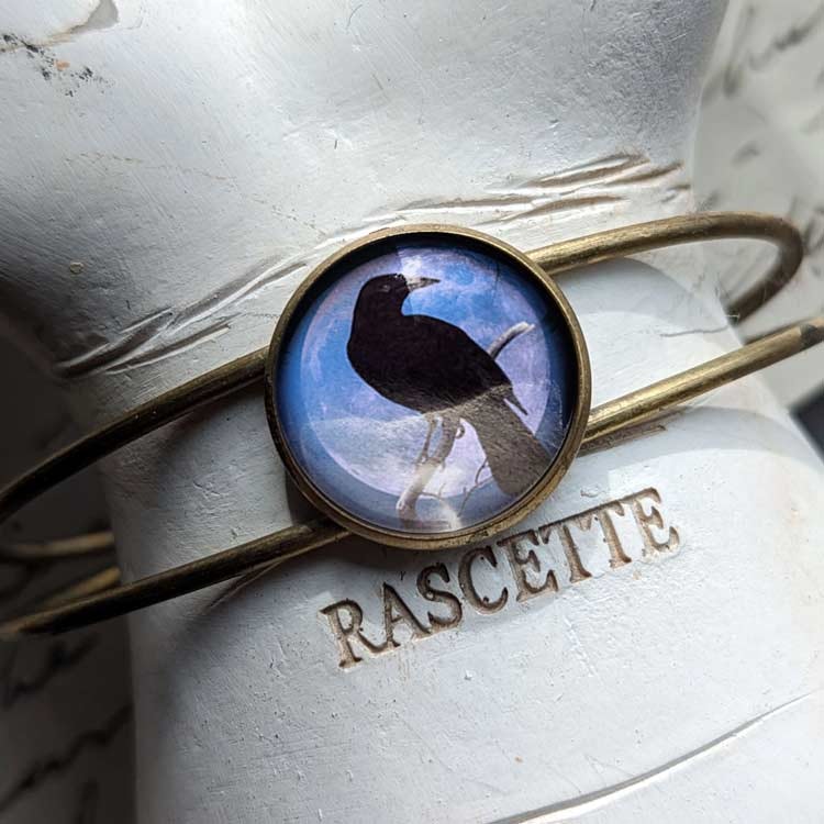 Vintageinspirerat manschettarmband med en illustration av en kråkfågel.