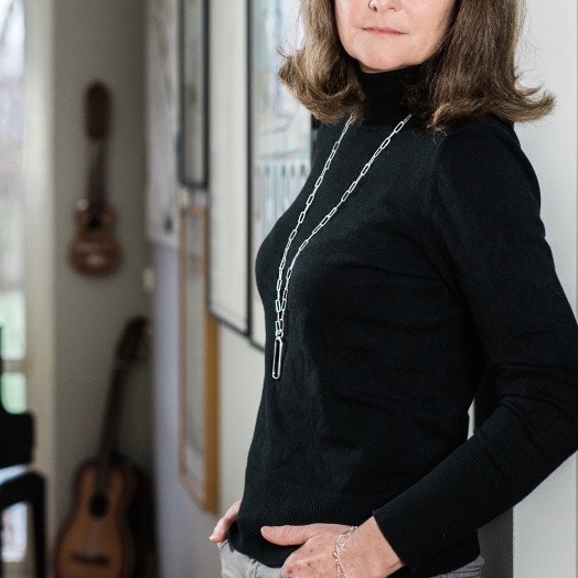 kvinna med lång silverkedja med rektangulära länkar, svarta kläder. woman with long silver chain with rectangular links around the neck, black clothing.