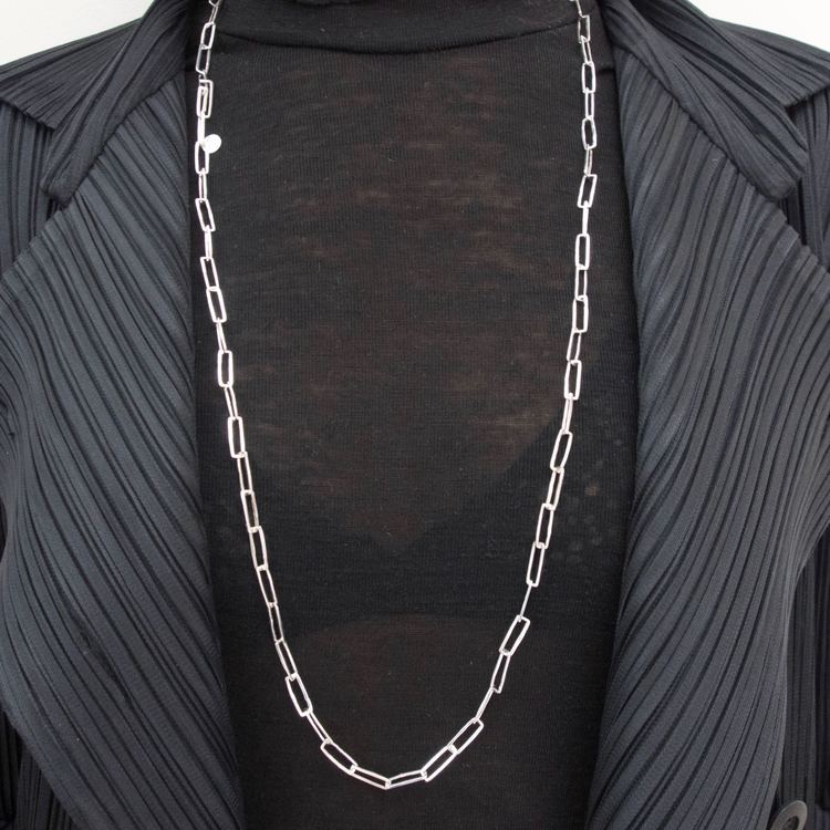 lång silverkedja med rektangulära länkar runt en hals med svarta kläder. long silver chain with rectangular links around the neck, black clothing.