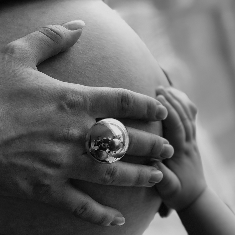 hand på gravid mage med stor silverring. hand on a pregnant stomach with a big silver ring.