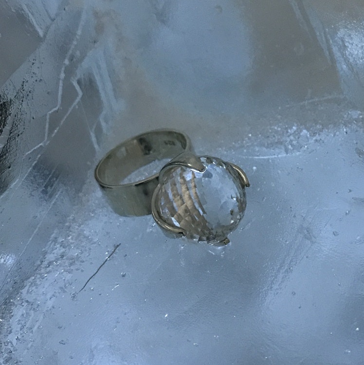 Stor silverring med en stor rund facettslipad bergskristall som ligger på is, från Ishotellet. big silver ring with crystal quartz on ice from the Ice hotel