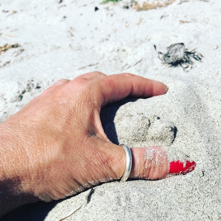 hand med slät silvering i sanden. hand with silver ring in the sand.