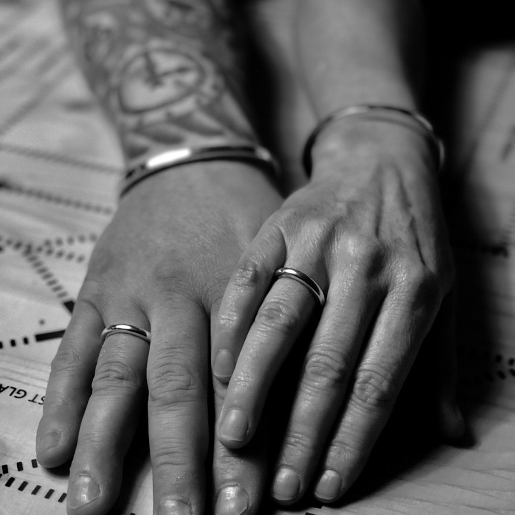 En manshand och en kvinnohand, bägge med samma unisexsmycken, släta silverringar och silverarmband med läder. man and women wearing the same jewelry, bracelets and silver rings, unisex.