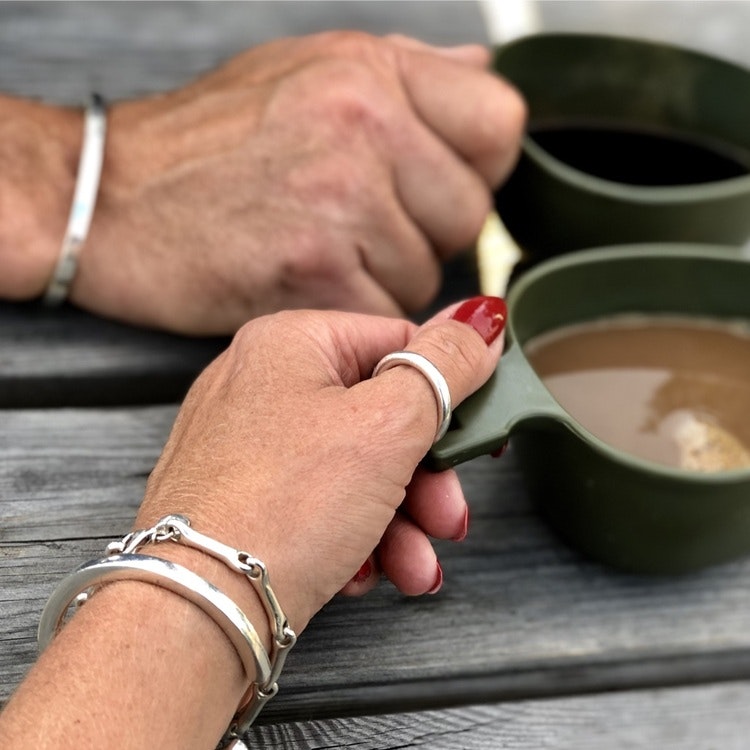 En manshand och en kvinnohand, bägge med samma unisexsmycken, silverring och armband. man and woman wearing the same jewellery, silver ring and bracelets.