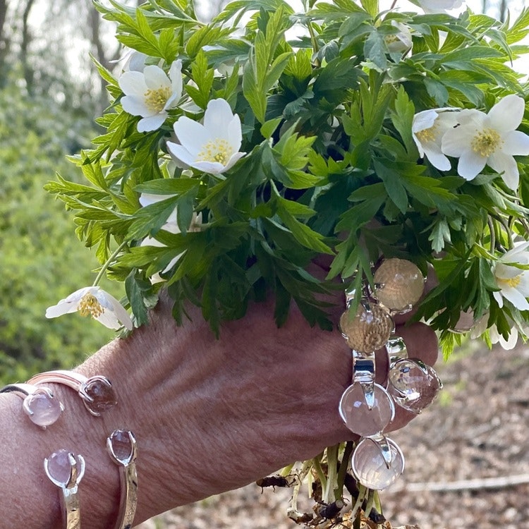 Hand med vitsippor och silverringar och armband, rosenkvarts och bergskristall.