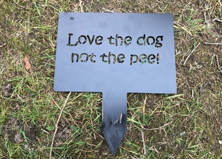 Liten skylt i stålplåt med texten love the dog not the pee, svatlackerad.