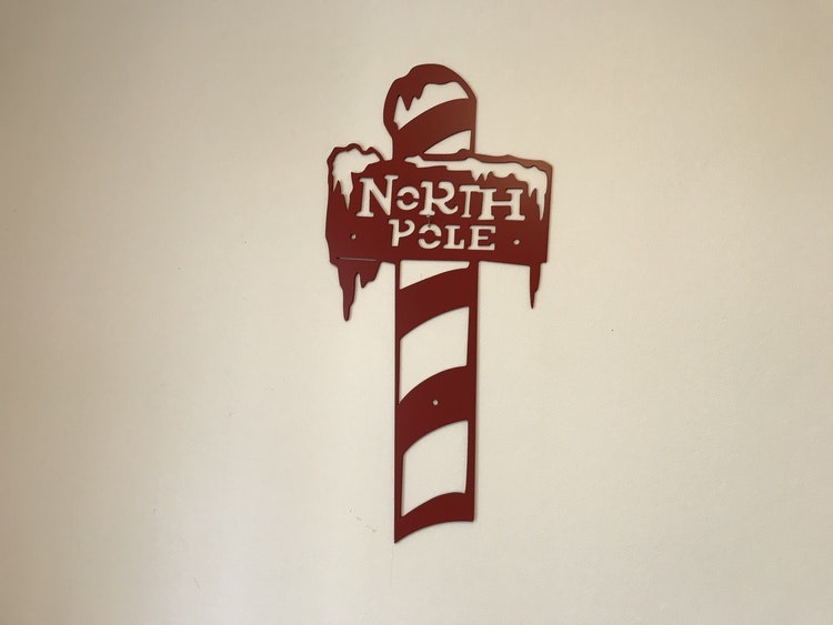 Röd stolpe i plåt med texten north pole att hänga på väggen.