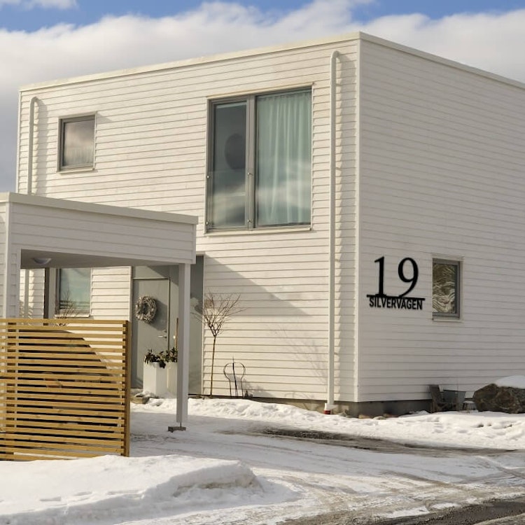 Stilrent husnummer med gatunamn, monterat på vitt modernt hus.