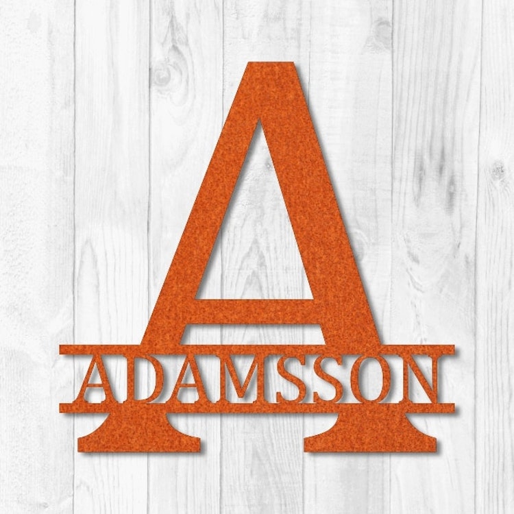 Personligt monogram i cortenstål mot vit träfasad.