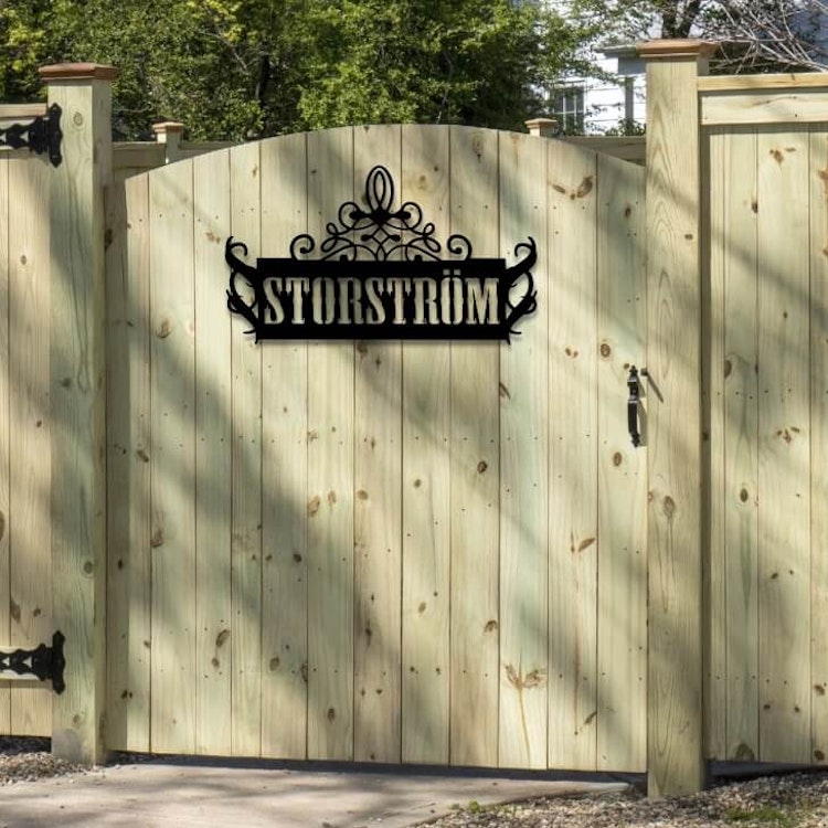Skylt i metall med eget namn monterad på trägrind.
