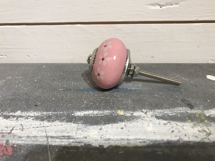 Rosa keramikknopp med blomrand på sidan.
