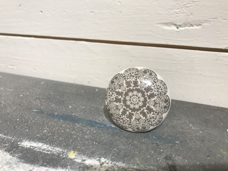 Vit knopp i keramik med grå blomma på framsidan.