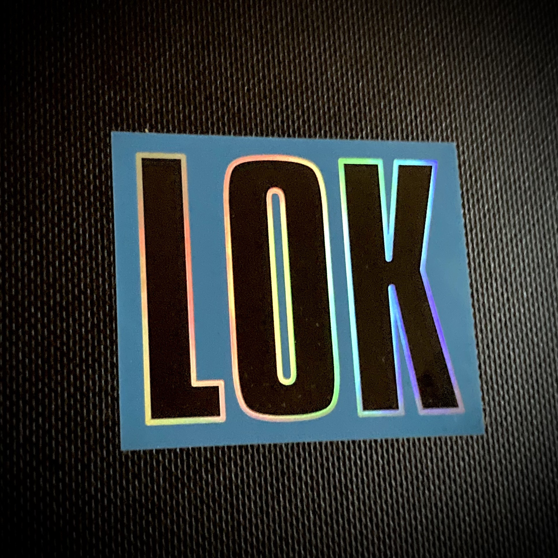 Klistermärke | LOK-loggan" (Svart logo + Holografisk Outline / Blå Bakgrund)