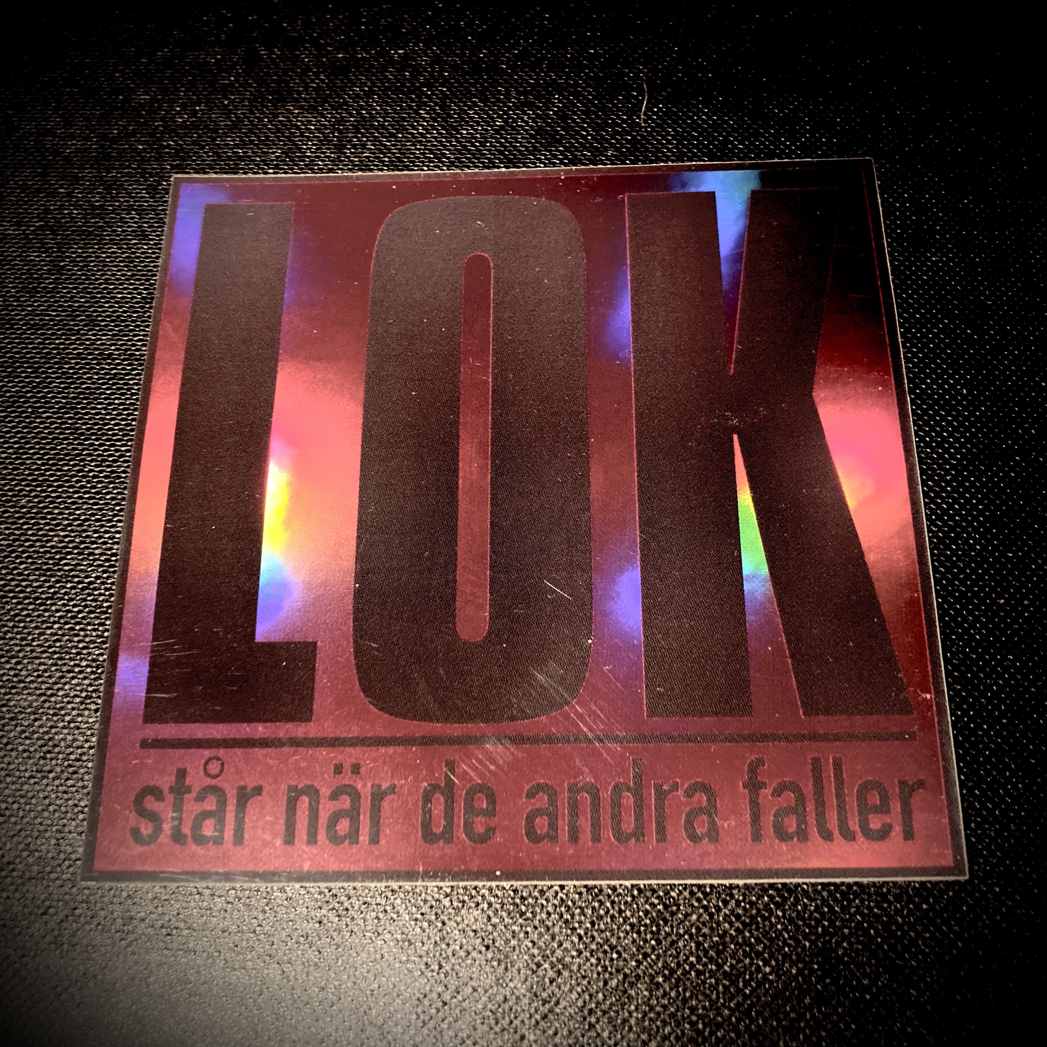 Klistermärke "LOK står när de andra faller" (Mörkgrå Logo / Rödtonad Holografisk Bakgrund)