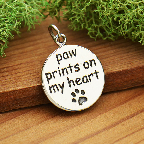 Bild på ett runt silverhänge med texten "paw prints on my heart"