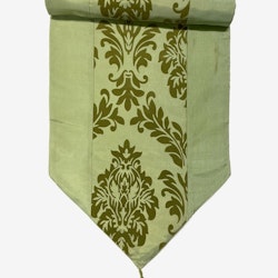 Oriental en ljusgrön bordlöpare i orientalisk stil med medaljongmönster i blanka textilier, mått 40 x 140 cm.