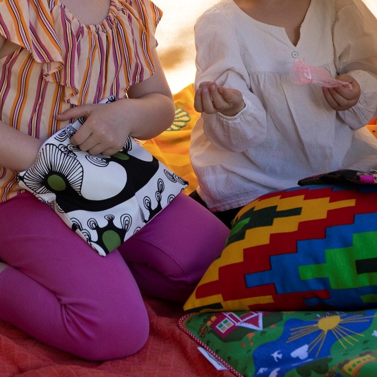 Barn i ett lektält fyllt av Magaloogi kuddar. Ett av barnen stoppar ner handen i en liten miniväska med dragkedja.