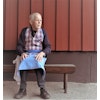 En ensam äldre man på en bänk. Iklädd förkläde "Köksan" skapat av minnestextilier från nära bortgången som han saknar.