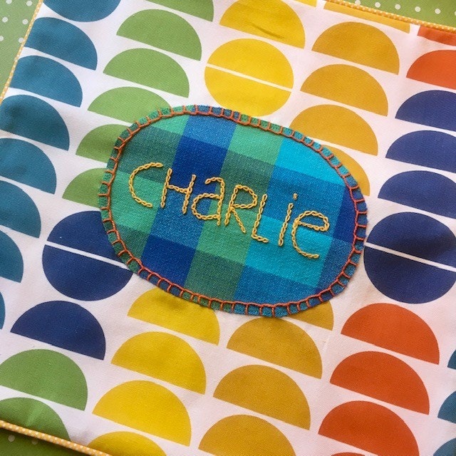 Närbild på kuddfodral med namnet Charlie broderat. Tyg i glada färger.