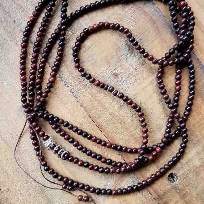 Långt halsband med små pärlor av mörk sandelträ & silverdetaljer.
