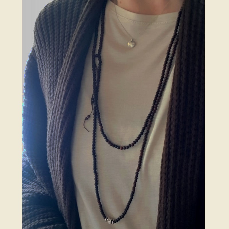 Långt halsband med små pärlor av mörk sandelträ & sju silverringar buret virat två varv.