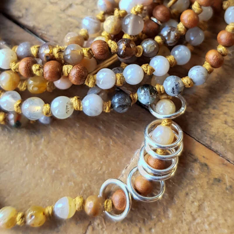 Sju mindre silverringar leker fritt på halsbandet, harmonierar fint med pärlorna i jordnära nyanser.
