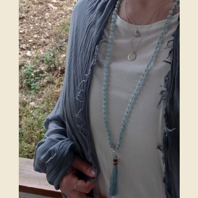 Mala halsband akvamarin med tofs av svensk lintråd, buret mot vit tröja lyfts de blå nyanserna i såväl pärlor som lintråd fram.