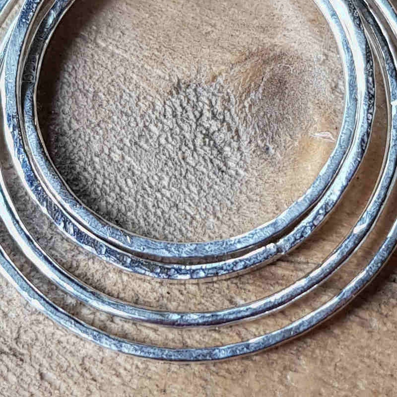 Närbild på silverhänge; fyra silverringar formade för hand, med lätt hamrad & bearbetad yta.