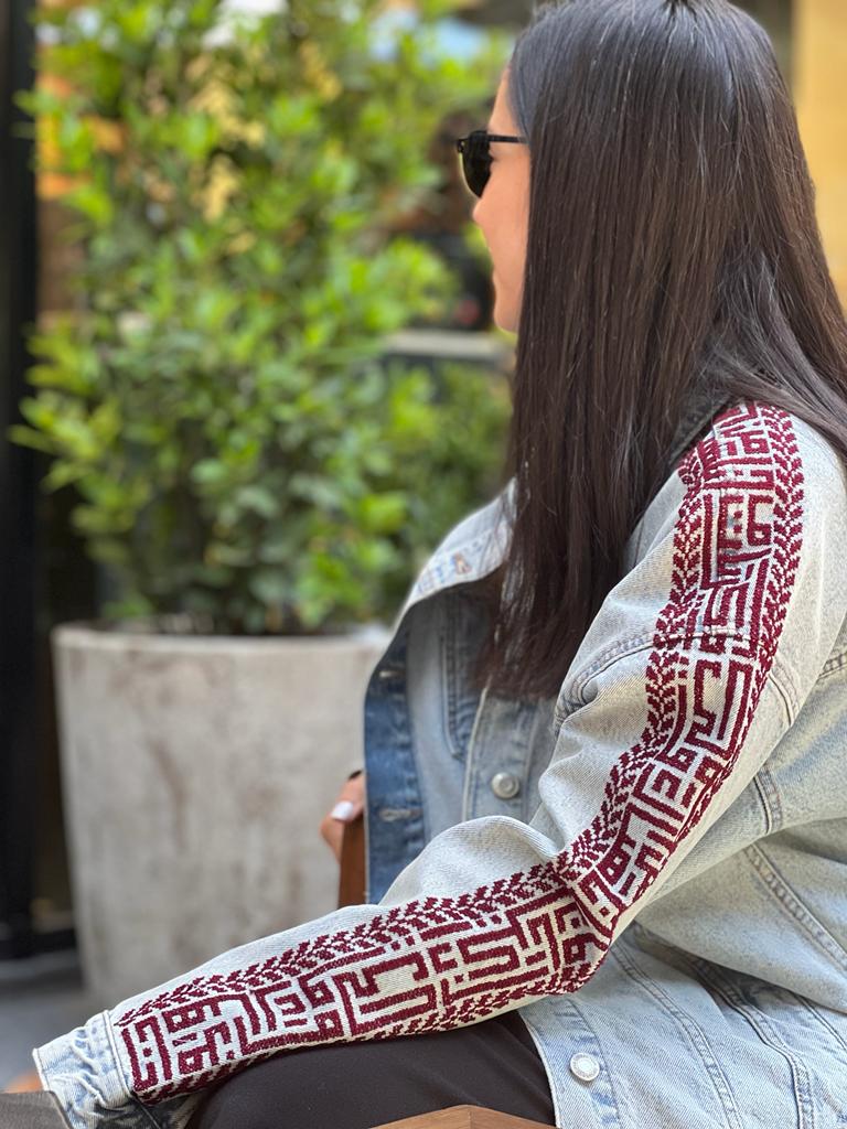 Darwish arm maroon & red denim jacket integrating poem verses from the prominent Palestinian Poet Mahmoud Darwish in cross-stitching on our Denim apparel.