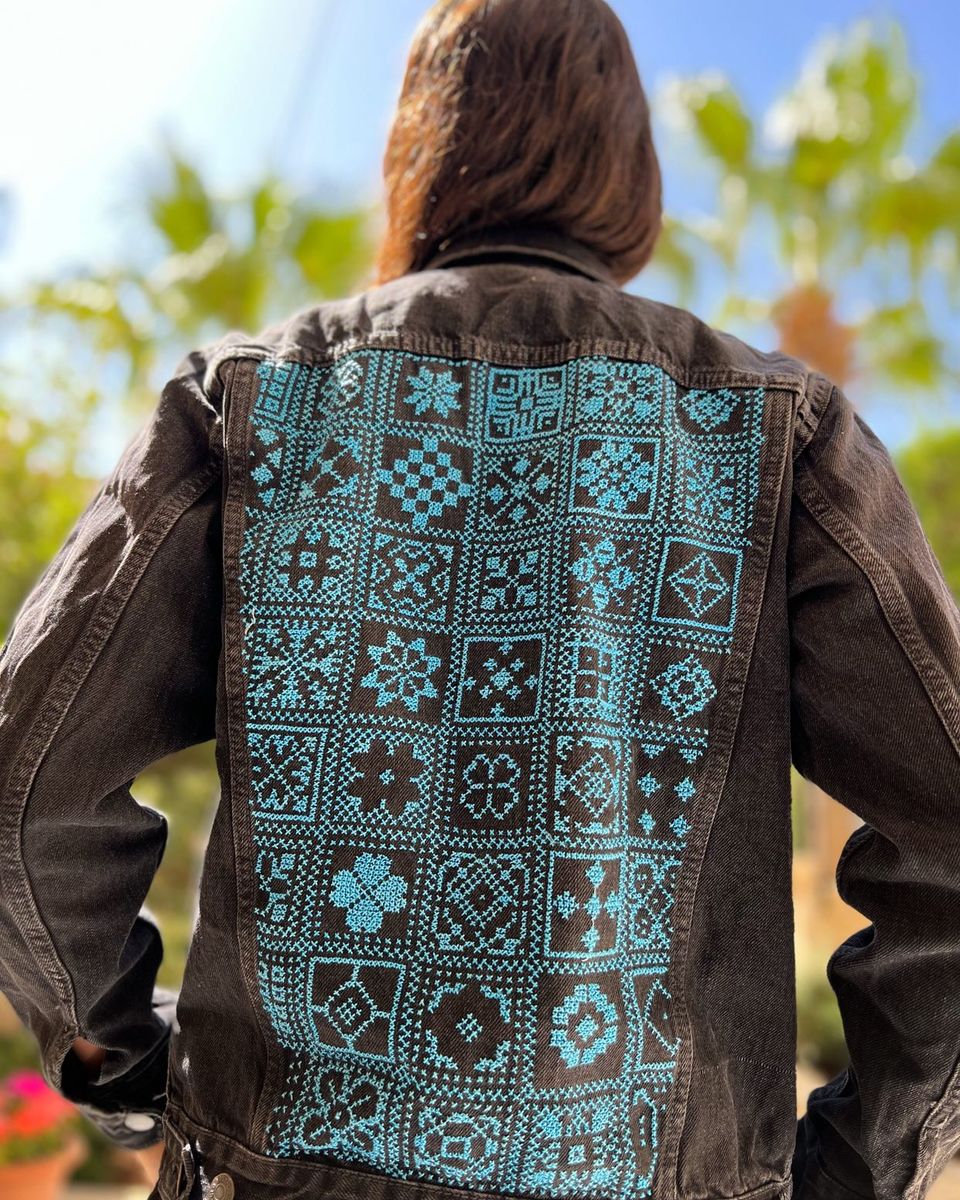 Arabesque in turquoise on black denim with long sleeves is hand embroidered with love in Jordan. Featuring patch pockets on the chest, welt pockets at the waist & a metal button fastening at the front
