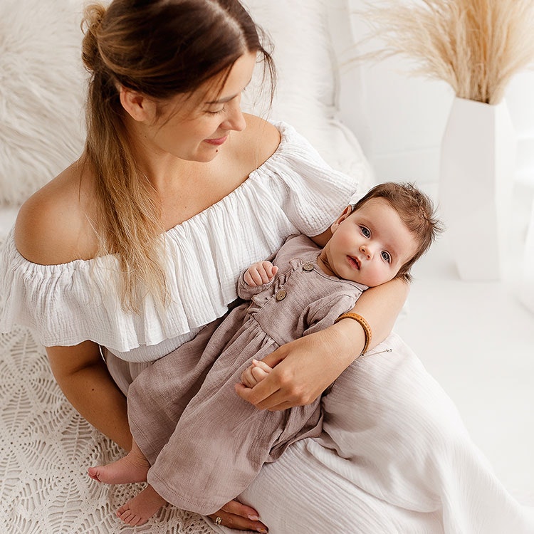 Mamma som håller i bebis i beige muslin klänning