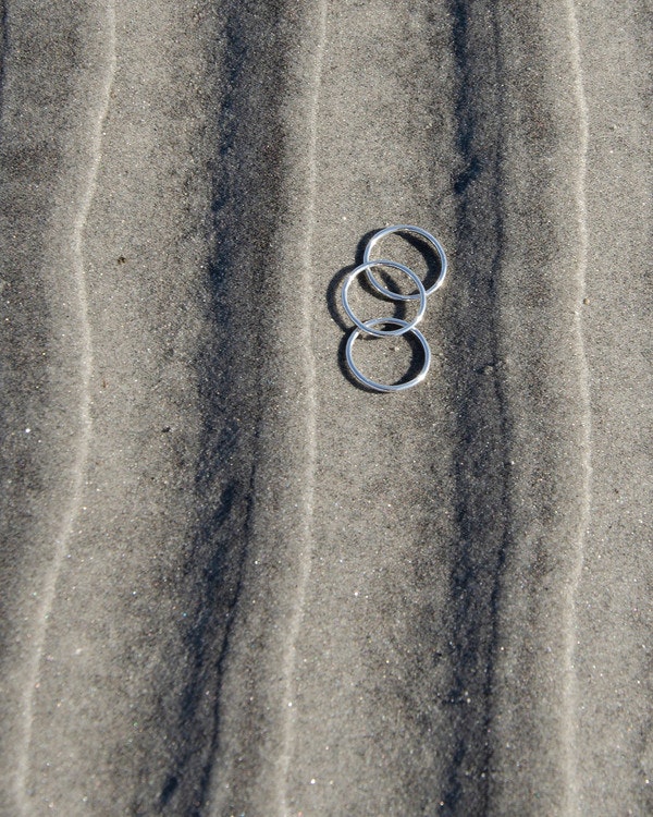 Handgjord enkel rund ring av äkta silver, 1,5 mm bred. Tre ringar ligger på stranden.