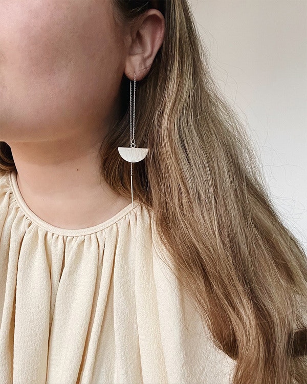 Handgjorda örhängen i silver, i form av en halvcirkel som sitter genom örat med en kedja. På modell.