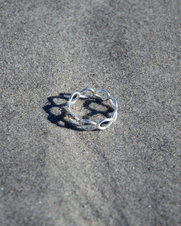 Ring i silver, med öglor ihopsatta som små böjda grenar. Ringen ligger på stranden.