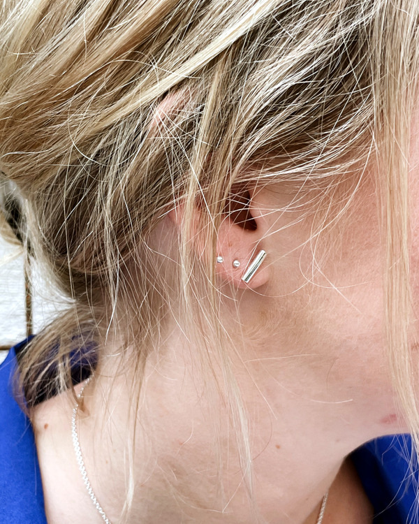 Litet silverörhänge med form av en rund stav. Bilden visar ett örhänge i örat.