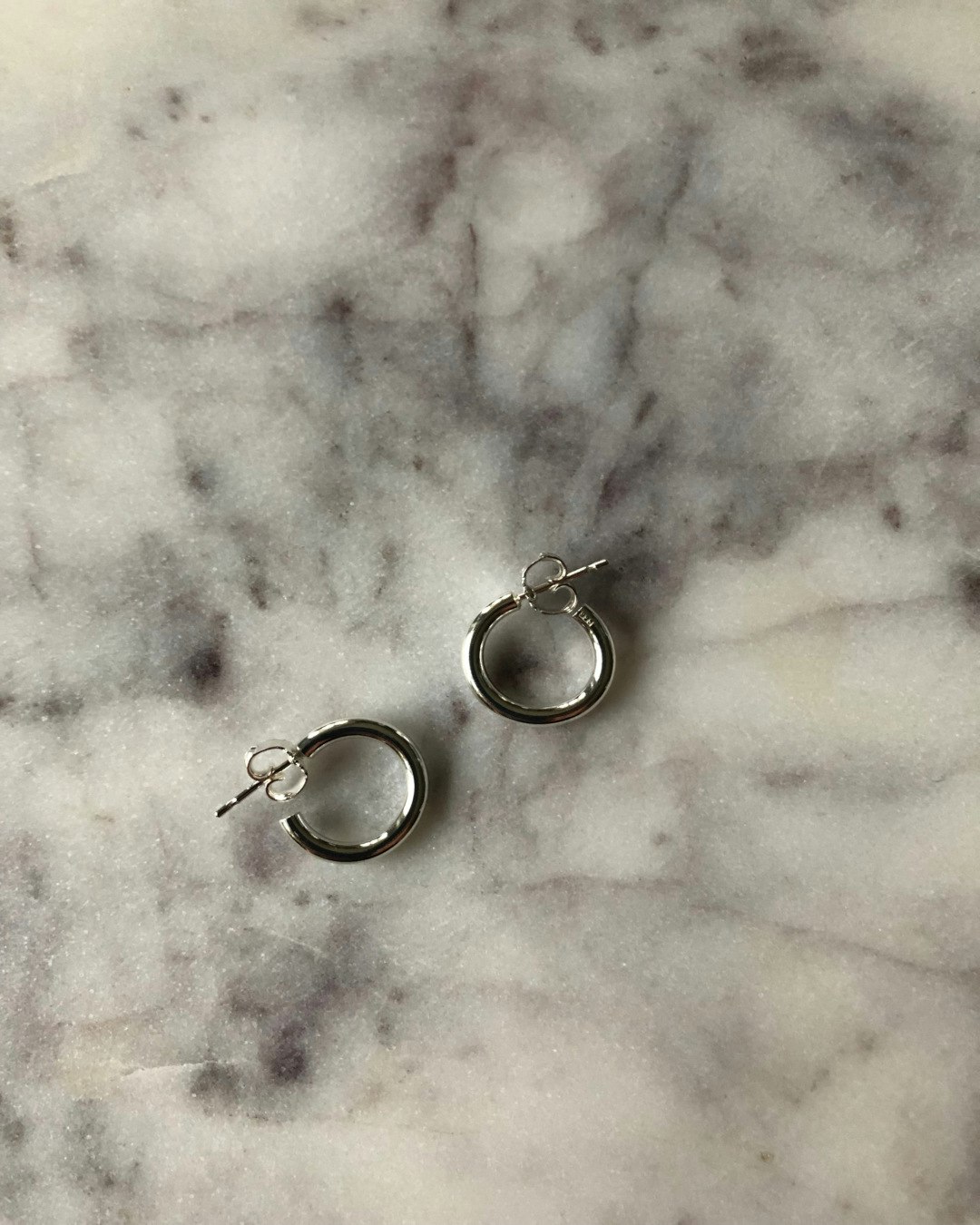 Enkla klassiska örhängen, små runda ringar i återvunnet silver. Ca 1,5 cm i diameter. Ett par örhängen på bord.