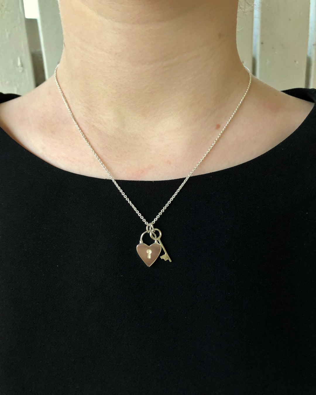 Handgjort halsband i återvunnet silver. I formen av ett hjärtformat hänglås och en nyckel. Halsbandet hänger runt halsen på tjej.