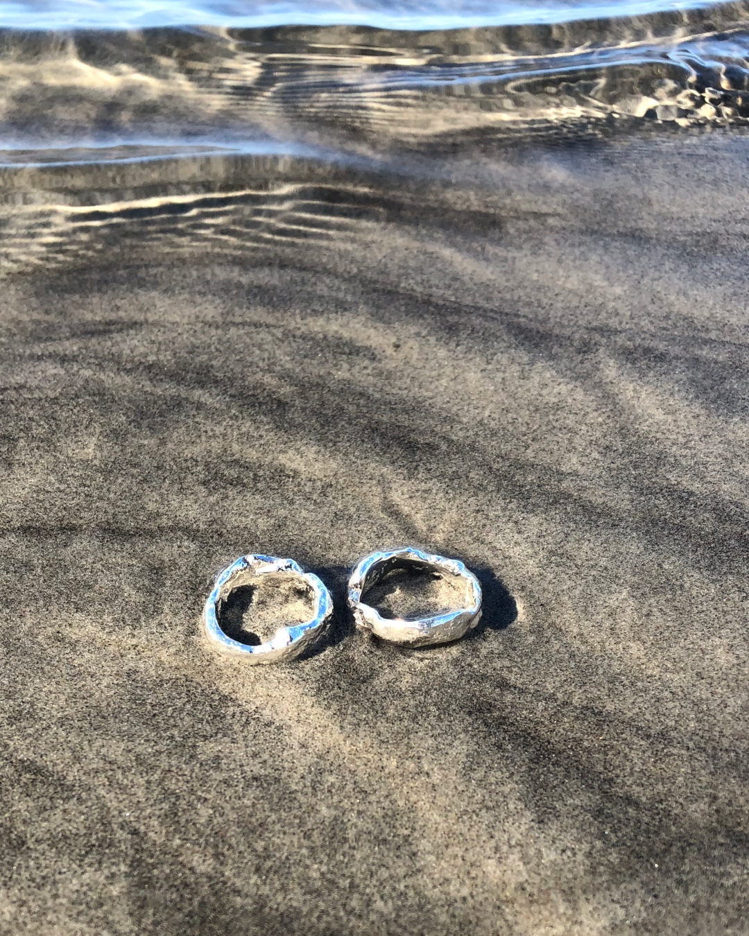 Kraftig oregelbunden ring av silver. Handtillverkad. Två ringar ligger på strand.
