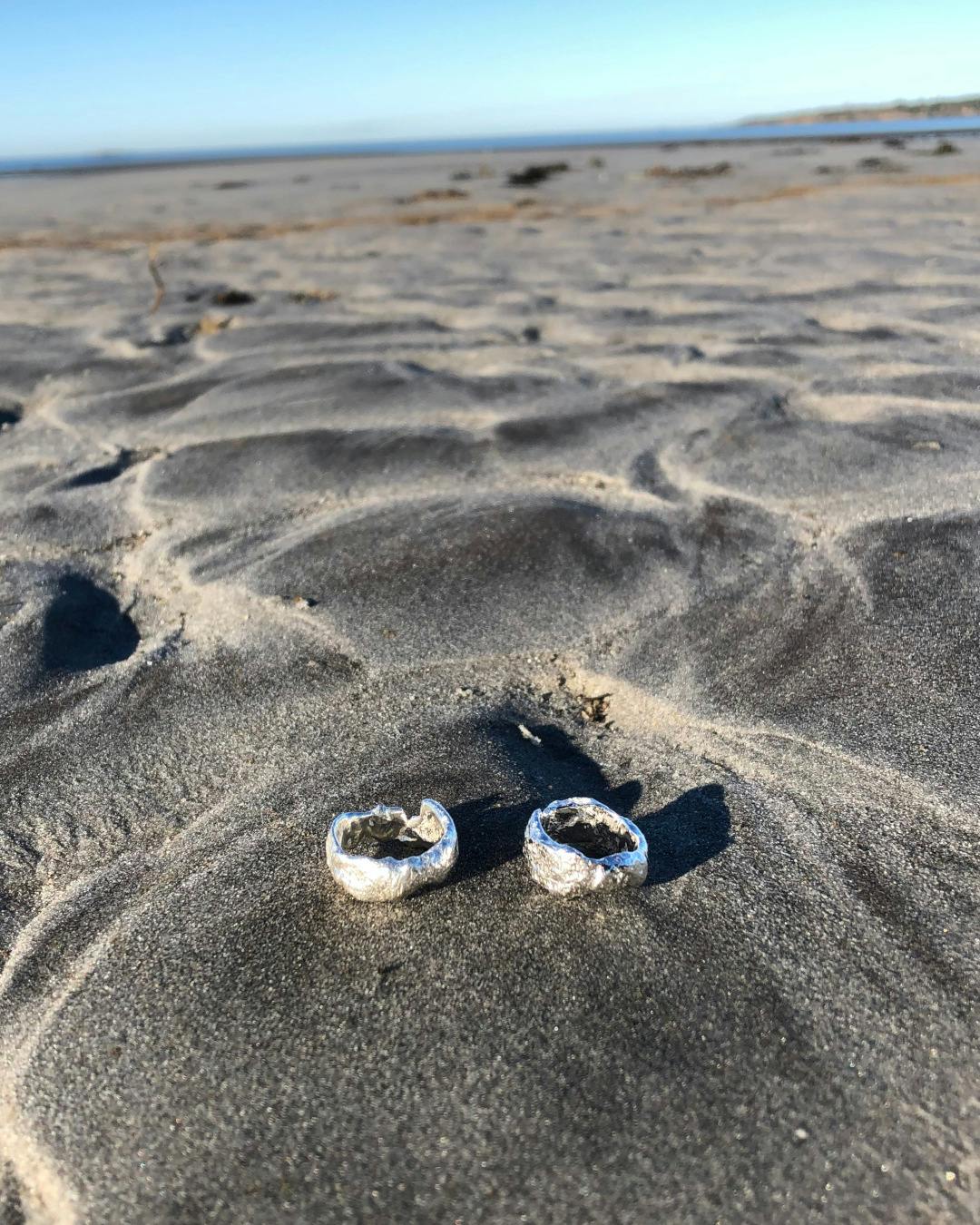 Kraftig oregelbunden ring av silver. Handtillverkad. Två ringar ligger på stranden.