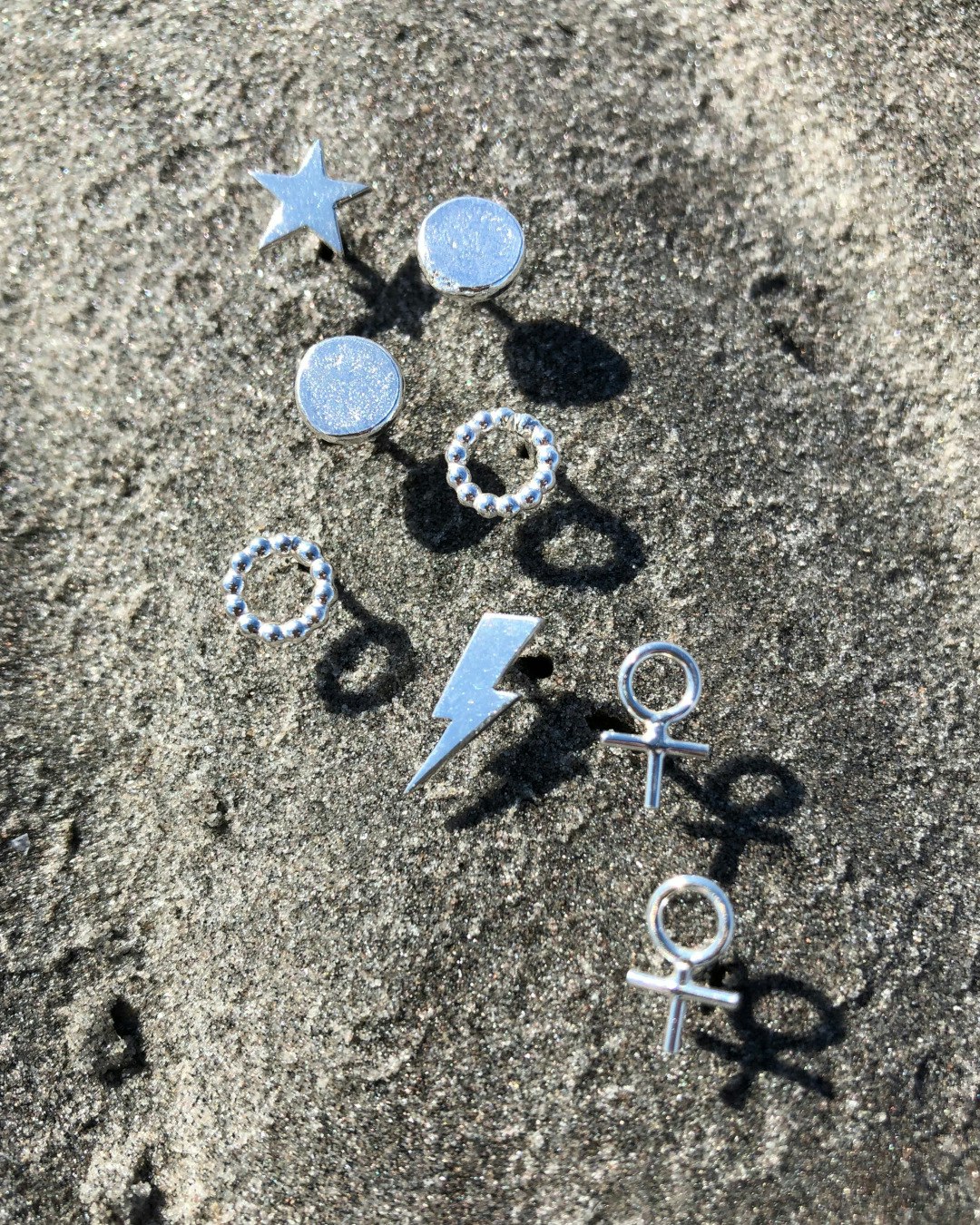 Litet örhänge, form av en kvinnosymbol. Flera örhängen på stranden tillsammans.