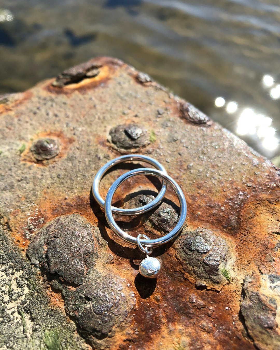 Handgjord ring i silver med hängande kula i silver, tillsammans med slät silverring.