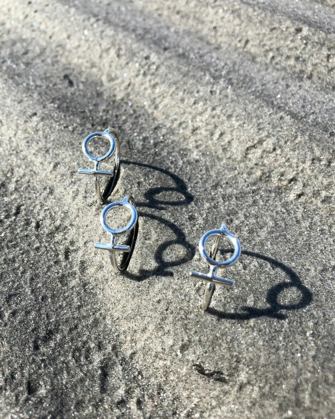 Silverring med kvinnosymbolen Venus. 3 stycken ringar ligger på sand.