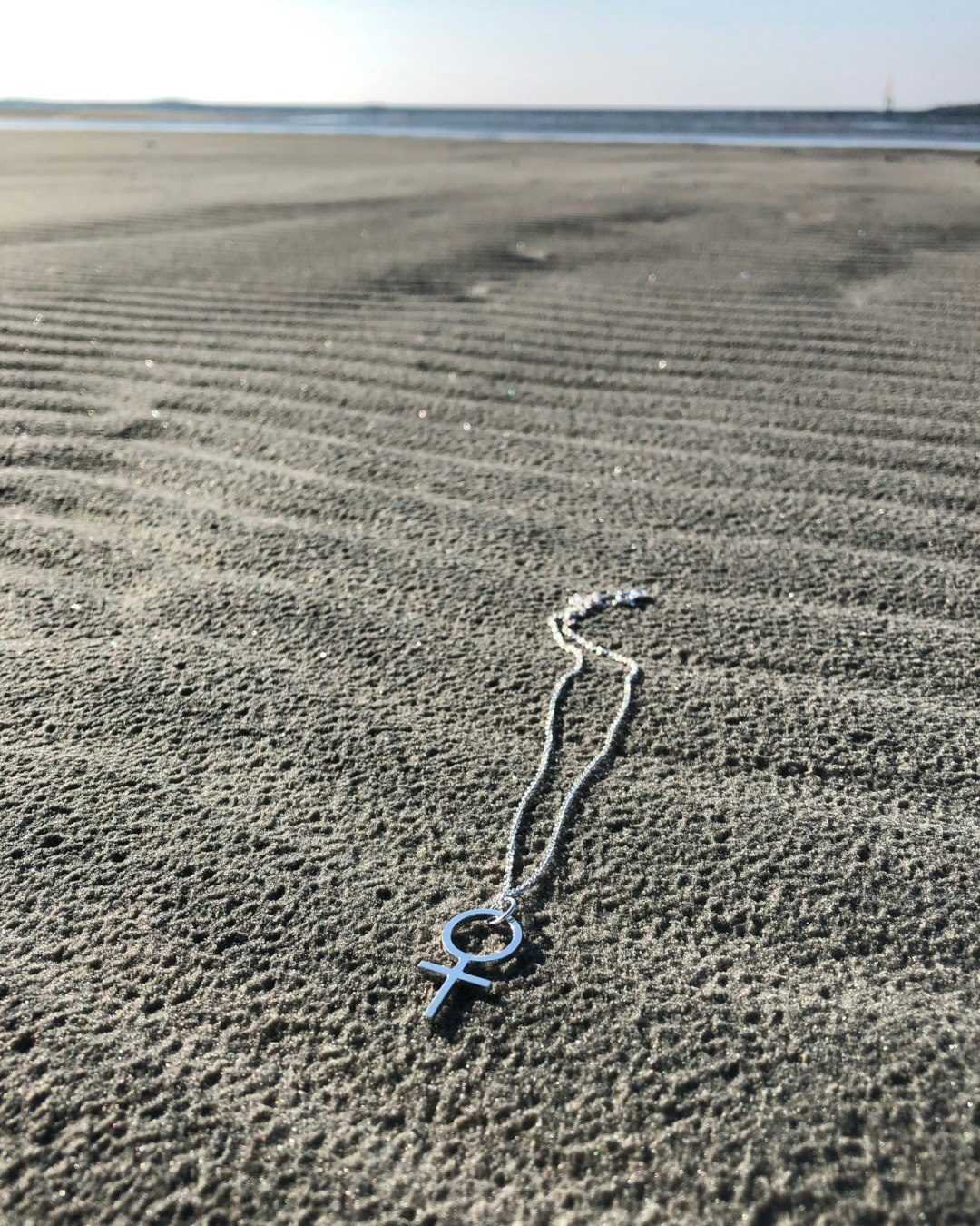 Kvinnosymbolen Venus som halsband. Ligger på stranden.