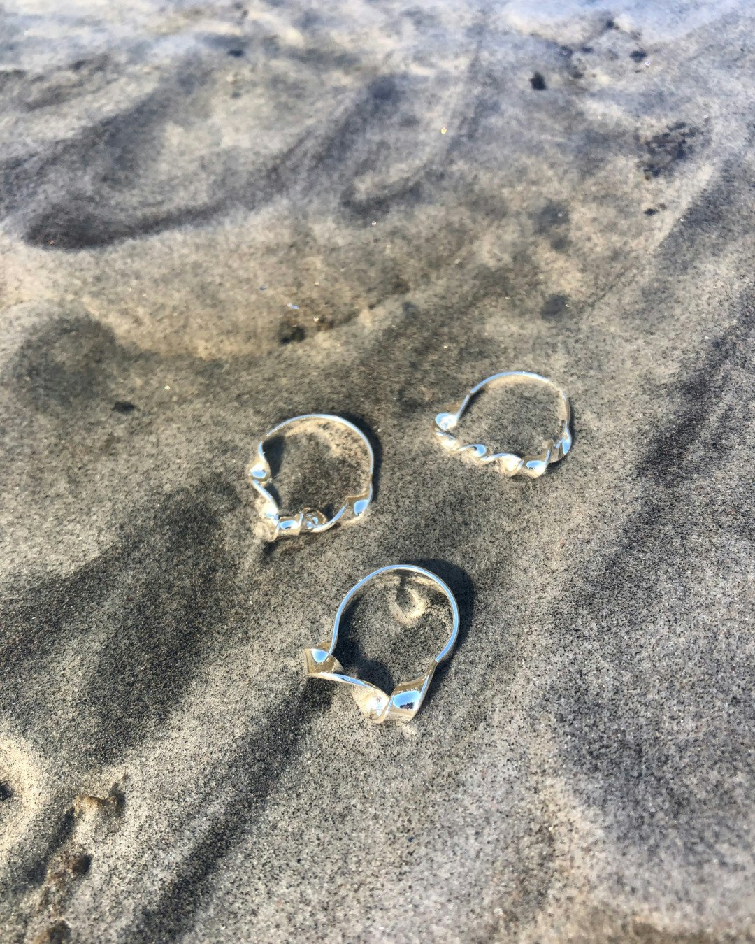 Ring i silver med vriden twist framtill. Tre ringar ligger i vattnet.