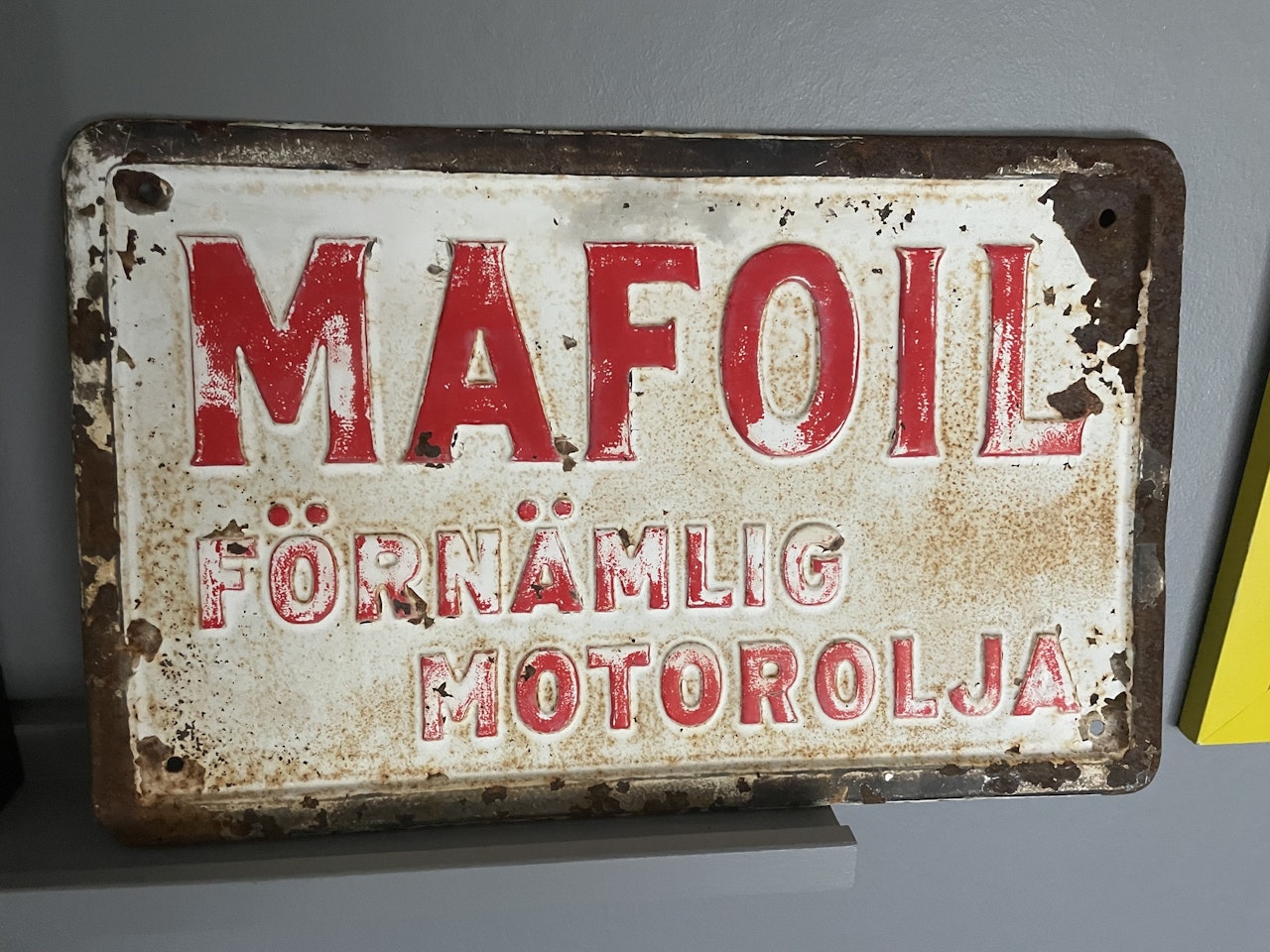 Plan och rektangulär skylt i litograferad plåt med prägling. Motivet är röd text ”Mafoil förnämlig motorolja” mot vit bakgrund med svart kant. Måtten är 350 x 220 mm. Skylten tillverkades under 1930-t