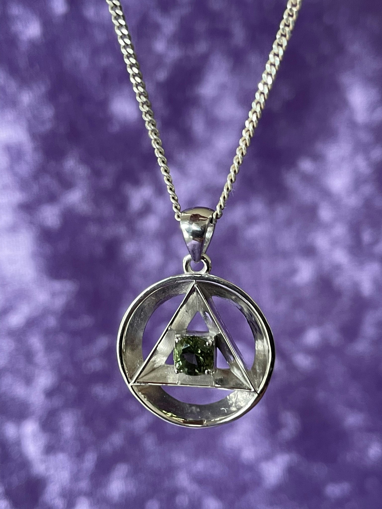 På bilden visas ett Moldavit smycke med Alkemistsymbolen i silver