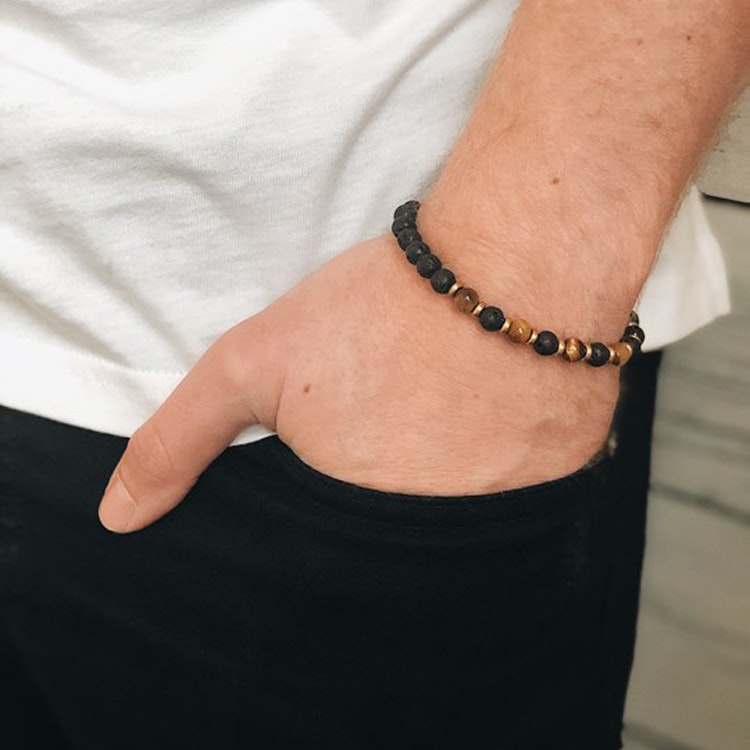 Ett beadsarmband i bruna, svarta och guldiga toner för herr- på modell.