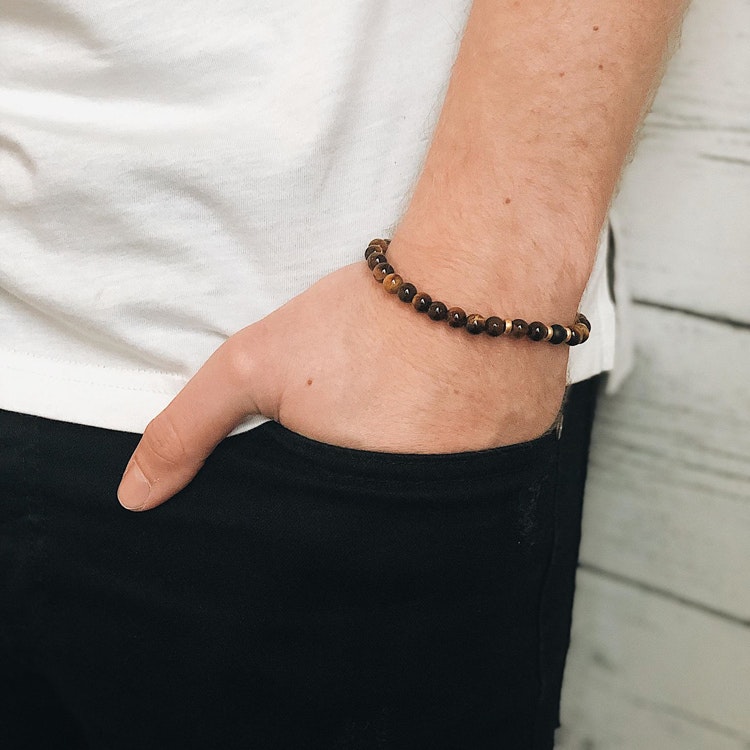 Ett beadsarmband med bruna, svarta och guldfärgade stenar för herr- på modell.