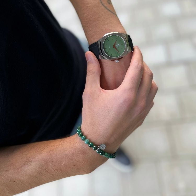 Ett grönt beadsarmaband för herr och grön klocka på modell.