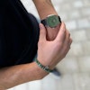 Ett grönt beadsarmaband för herr och grön klocka på modell.